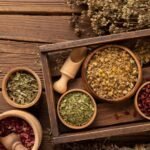 Rustic wooden box and bowls filled with dried herbs and spices on a weathered wooden table.