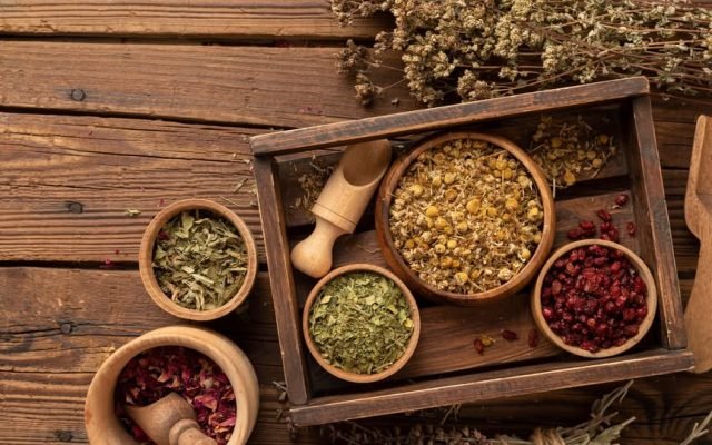 Rustic wooden box and bowls filled with dried herbs and spices on a weathered wooden table.